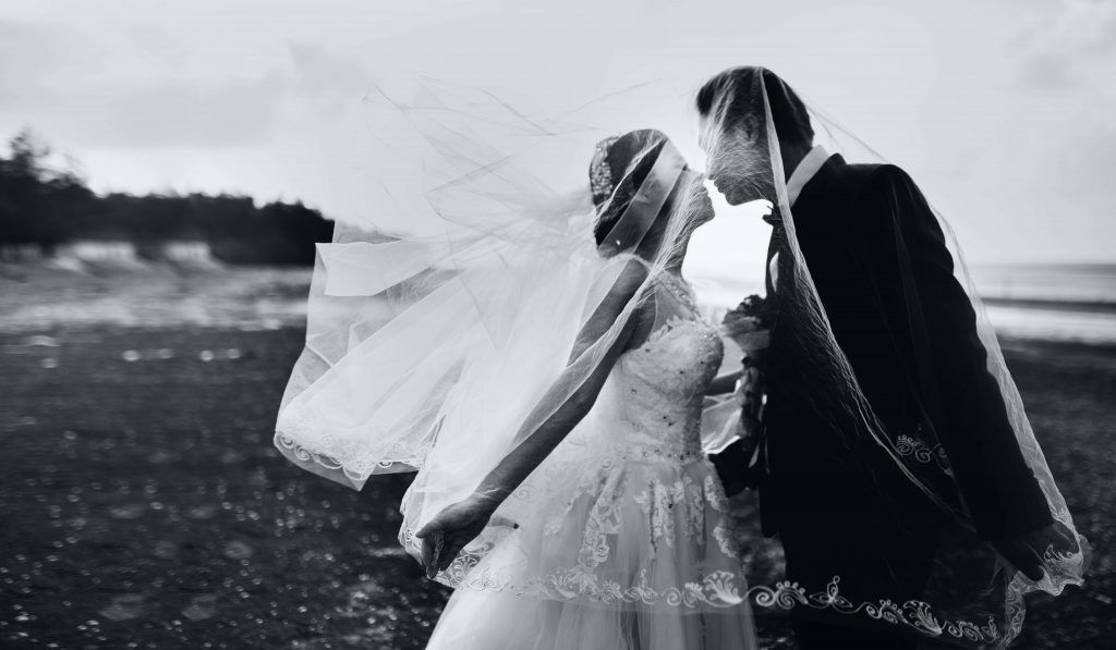 Pareja de novios besándose bajo un velo bodas Covid19